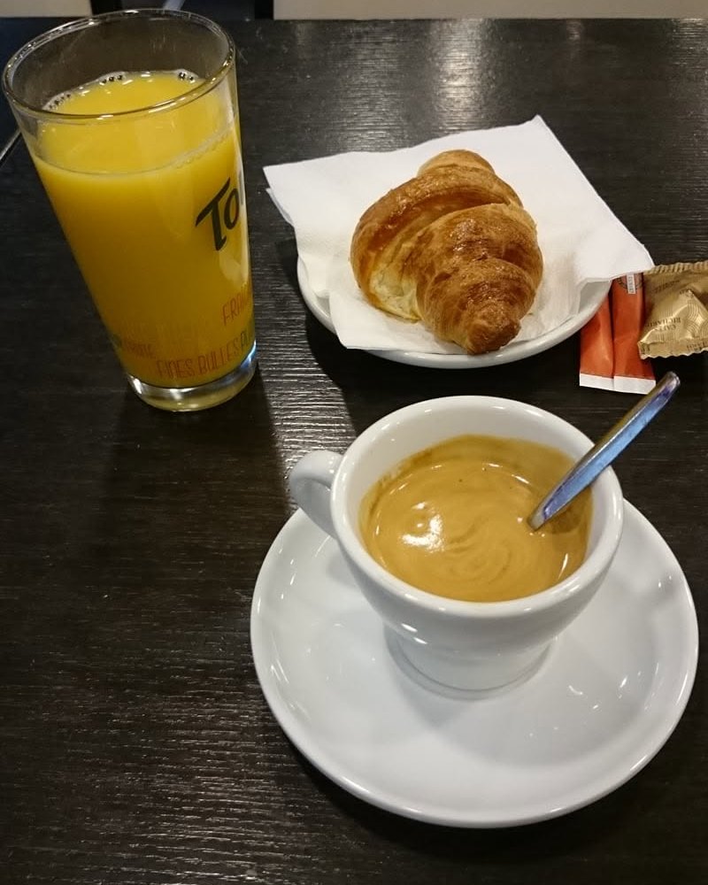 Petit-déjeuner servi au Dauphin : un café expresso, un croissant doré et un jus d’orange frais sur une table de la salle.
